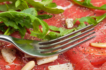 Carpaccio auf einem Teller mit Parmesan und Pinienkernen