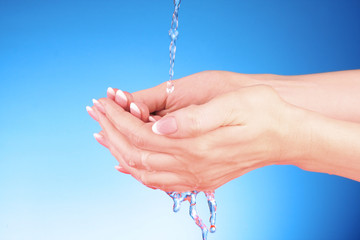 Naklejka na ściany i meble Human hands with water splashing on them with blue background