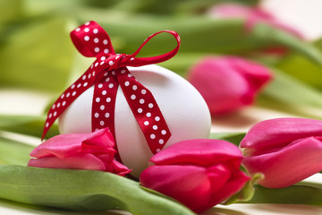 Osterei mit gepunkteter roter Schleife vor Tulpen