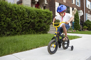 Young boy riding his first bicycle with training wheels