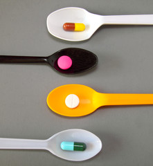 four spoons with different pills on grey background
