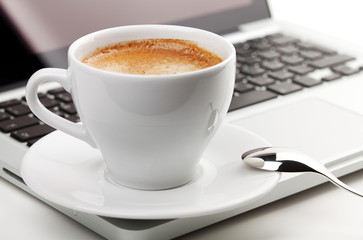 Cappuccino cup with spoon on laptop