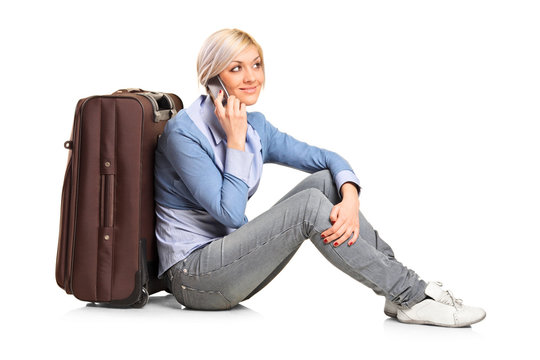 Tourist girl seated next to a suitcase talking on mobile phone