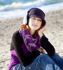 Portrait of red-haired girl in cap with headphone on the beach.