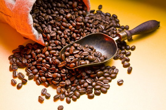 Sack of coffee beans and scoop. On a dark yellow background.