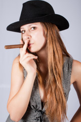 Portrait of the beautiful and stylish girl in a hat with a cigar