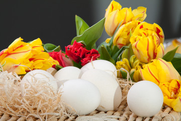 Yellow and red tulips with white eggs lying on a straw tray