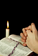 Open Bible with burning candle and hands of praying woman