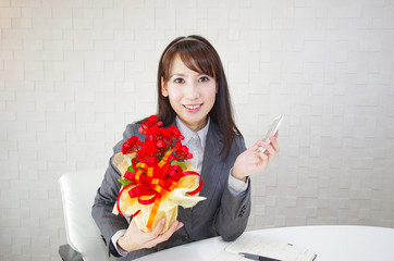 プレゼントの花を持った笑顔のオフィスレディー