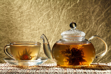 Glass teapot and a cup of green tea on a gold background