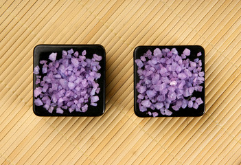 Two black bowls filled with purple salt on a bamboo mat