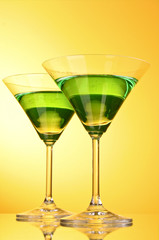 glass with a green alcoholic beverage to a yellow-brown backgrou