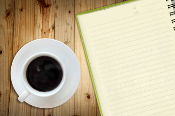 White cup of hot coffee and white sketch book on wood table