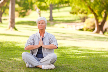 Naklejka na ściany i meble Senior woman practicing yoga in the park