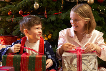 Fototapeta na wymiar Children Opening Christmas Present In Front Of Tree