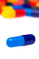 One blue capsule in front of many colorful