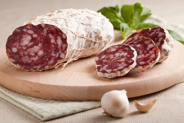 Traditional sliced salami on wooden board with garlic and herbs