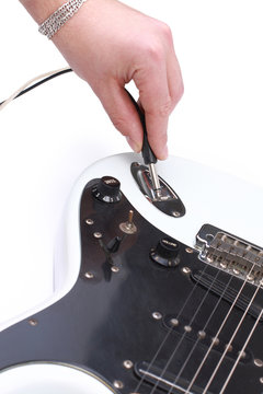 Person tuning a guitar from its headstock over white
