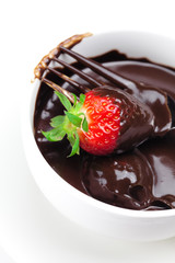 melted chocolate in a cup, fork and strawberries isolated on whi