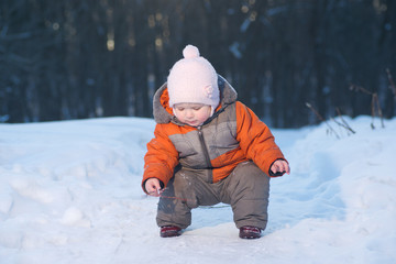 Adorable baby picking up small tree branch on snow road in park