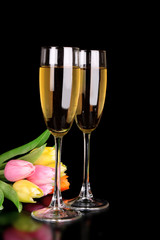 Glasses with champagne on black background with tulip flowers