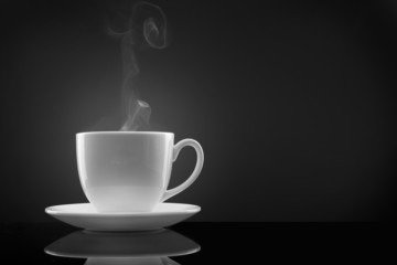 white cup with hot liquid and steam on black