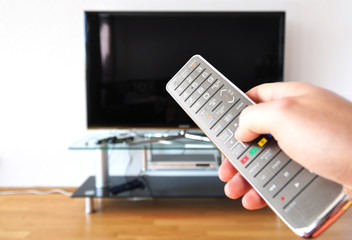Remote control in the hand against TV screen