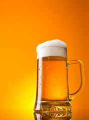 Glass of beer close-up with froth over orange background