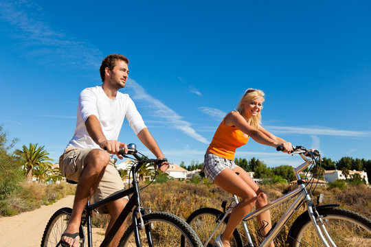 Couple In Holidays Cycling On Beach