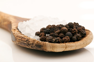 Coarse salt and pepper corns on wooden spoon on white background