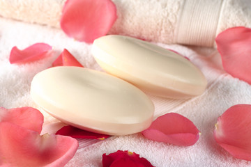 Two soap bars on towels with pink and red rose petals