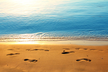 footprints on sand along sea at dawn