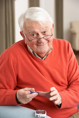 Senior Man Checking Blood Sugar Level At Home