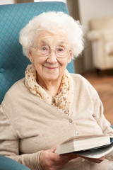 Senior Woman Relaxing In Chair At Home Reading Book