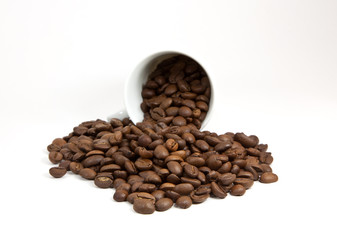 Overturned cup with coffee beans on white background