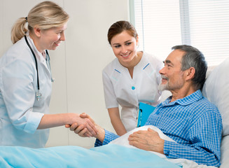 doctor shakes hands with patient in hospital bed