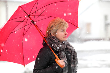 Woman with red umbrella in a winter day while snowing