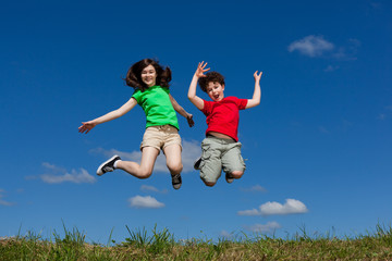 Girl and boy jumping, running against blue sky