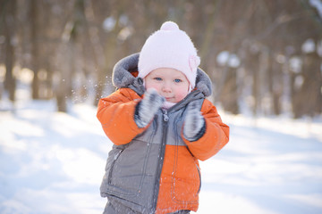 Fototapeta na wymiar Adorable baby clapping with mittens in sunny winter park