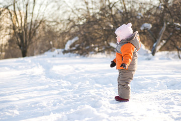Fototapeta na wymiar Adorable baby stay on road on hill side in winter sunny park