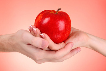 Apple between man and woman hand on red background