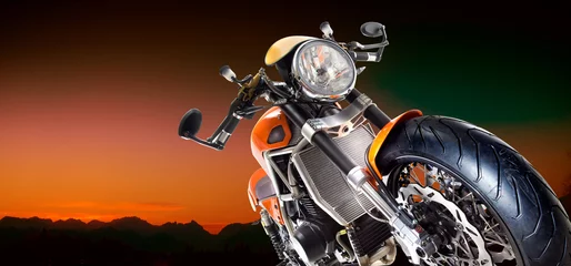 Photo sur Aluminium Moto Moto sous un ciel orange et fond de montagnes.