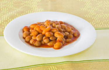 Cooked haricot beans with tomato sauce on a white plate.