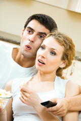 Young couple eating popcorn and watching TV at home