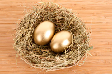 Three golden hen's eggs in the grassy nest on the wooden table