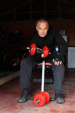 Middle Aged Man Working Out In Garage Gym With Dumbells