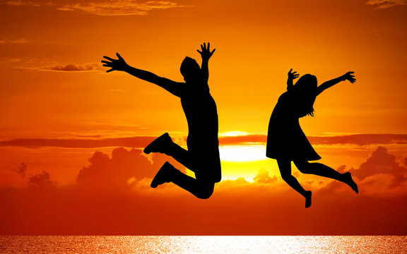 Silhouettes of couple jumping on sunset background
