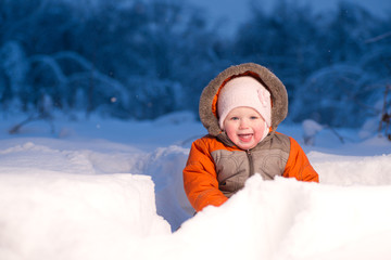 Adorable baby sit and digging hideout hole in snow in field in t