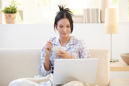 Girl in pyjama having cereal using laptop