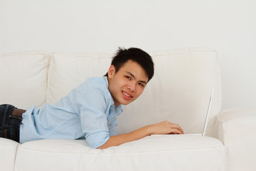 A man lying prone using his laptop on a sofa
